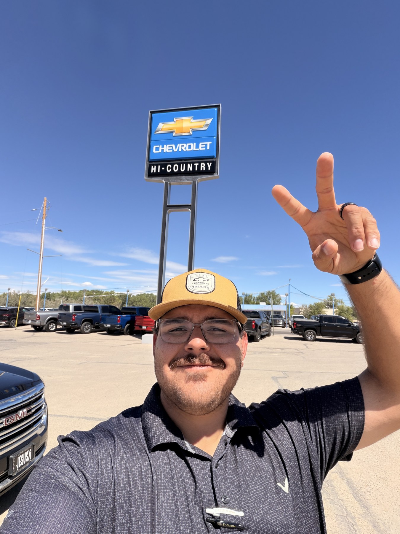 Zach ‘Tank’ Charles outside Hi Country Chevrolet, with a peace sign and a lot full of trucks.